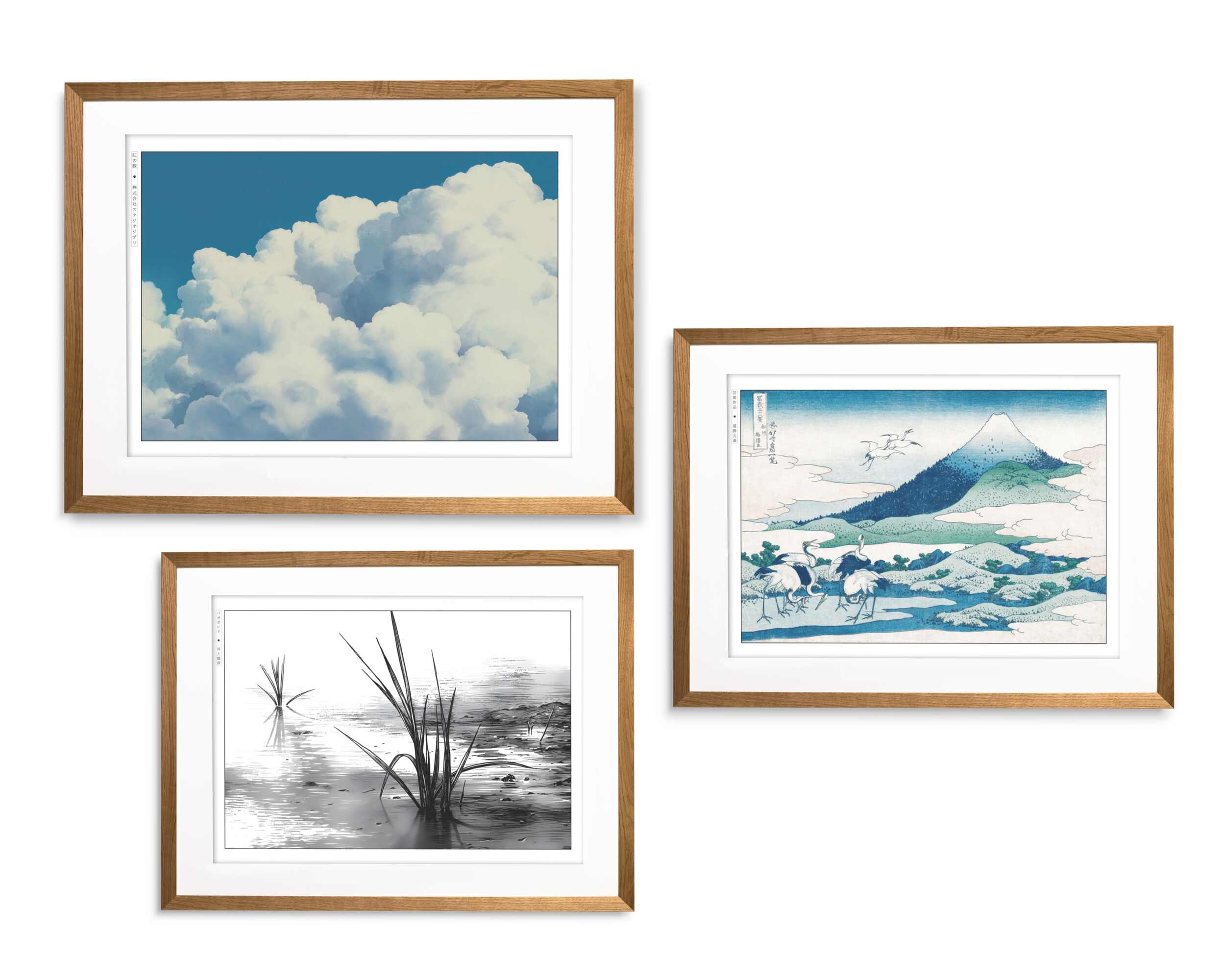 Gallery wall of framed art prints in oak frames showing clouds, a monochrome ink landscape, and a Mount Fuji scene with birds